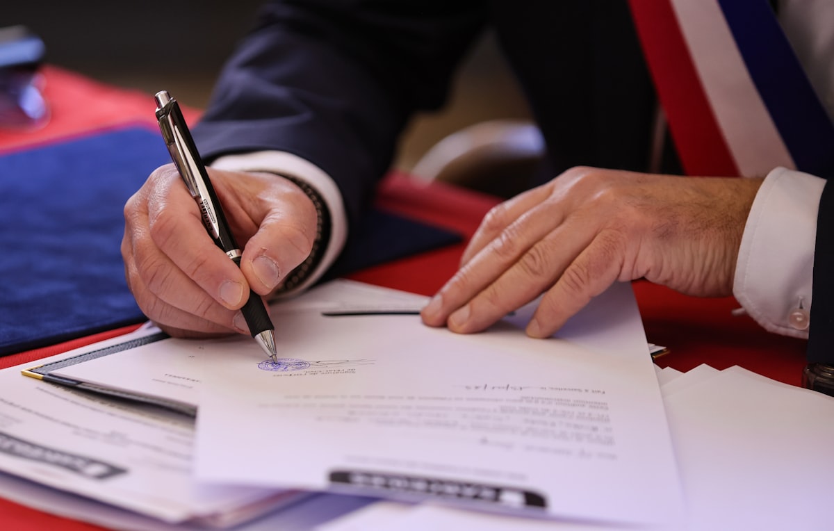 Close-up of a person in a suit signing legal paperwork at a desk with a pen